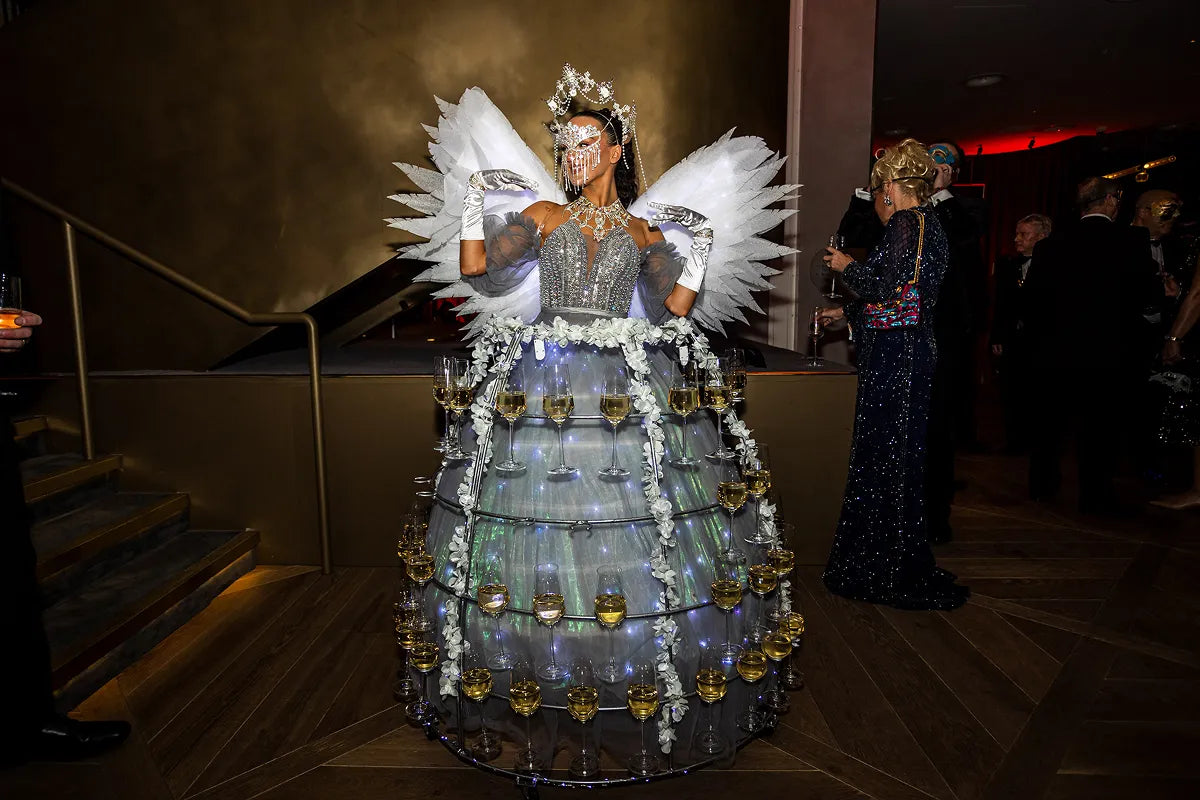 A performer in an illuminated dress cage filled with champagne glasses at the London New Year's Eve Masquerade