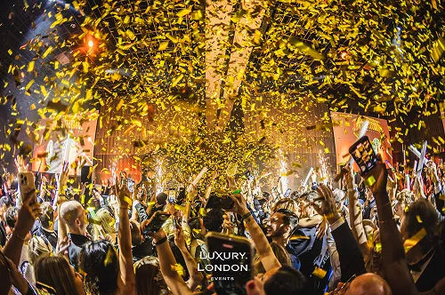 A crowd of guests celebrating under a massive shower of golden confetti at the London New Year's Eve Masquerade